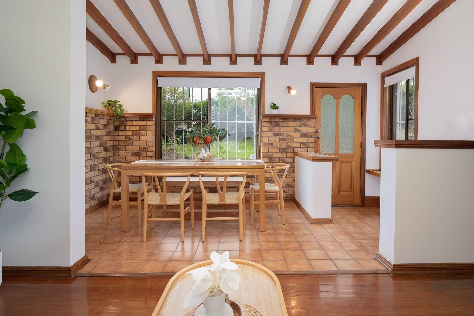 Una cocina con una mesa y sillas, pared de ladrillo, puerta de madera y ventana con vista a la vegetación.