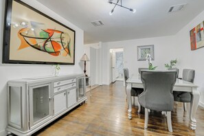 A dining area with a white table, gray chairs, a cabinet with glass doors, and a large abstract painting on the wall. - Charming 3-bedroom house with AC in Anahuac (Anahuac)