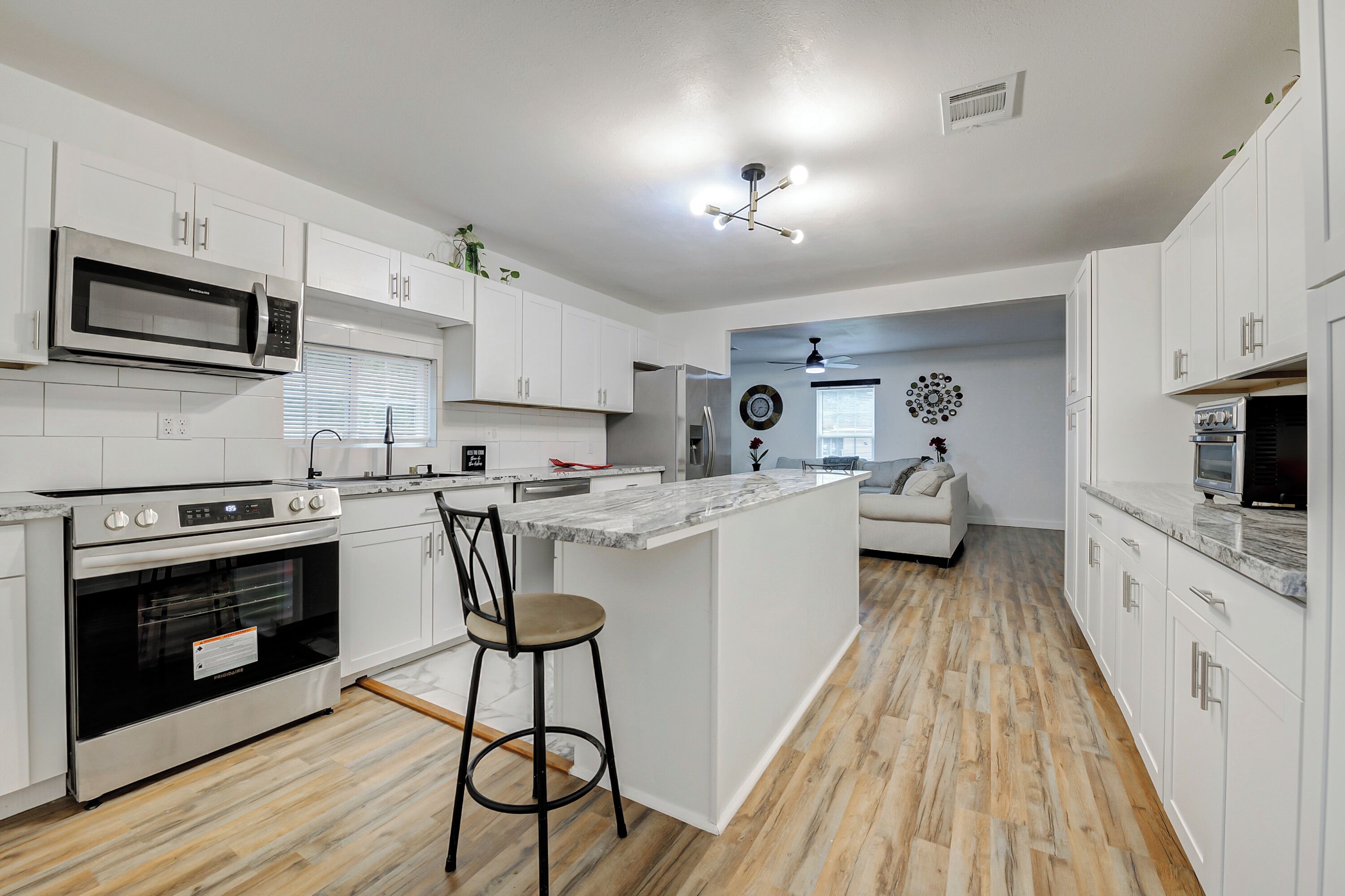 A modern kitchen with white cabinets, a built-in microwave, a stove, and a bar stool.