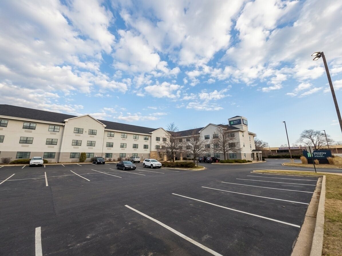 A parking lot with several cars, a building with multiple windows, and a sign indicating a hotel.