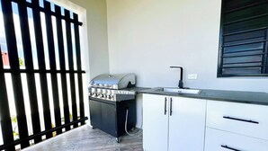 A compact kitchen with a built-in grill, a sink, and a window with blinds. - Solana Apartments  (Nadi)