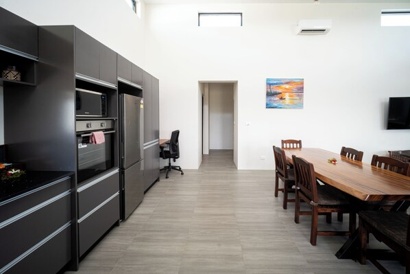 A modern kitchen with built-in appliances, a dining area with a wooden table and chairs, and a painting on the wall.