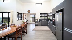 A modern kitchen with dark cabinets, a stainless steel refrigerator, and a dining area with a wooden table and chairs. - Solana Apartments  (Nadi)