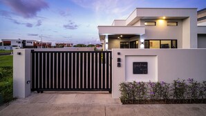 A modern villa with a gated entrance, a sign indicating 'grifna Villas 24,' and a well-maintained lawn.