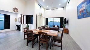 A spacious dining area with a high ceiling, large windows, and a view of the sea.