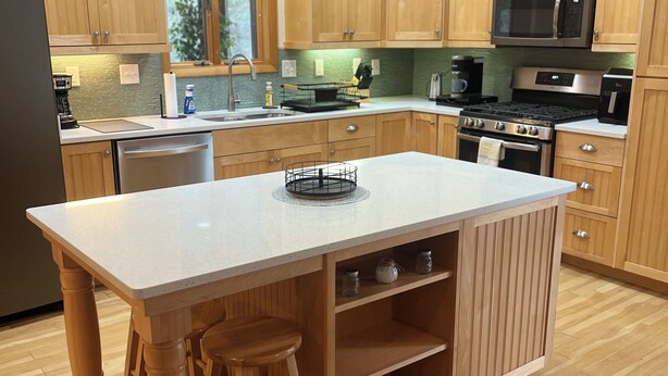 Una cocina con armarios de madera, un refrigerador de acero inoxidable, un microondas, una estufa y una isla grande con taburetes.
