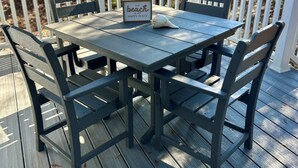 Una terraza de madera con una mesa, sillas, un letrero enmarcado y una concha marina.