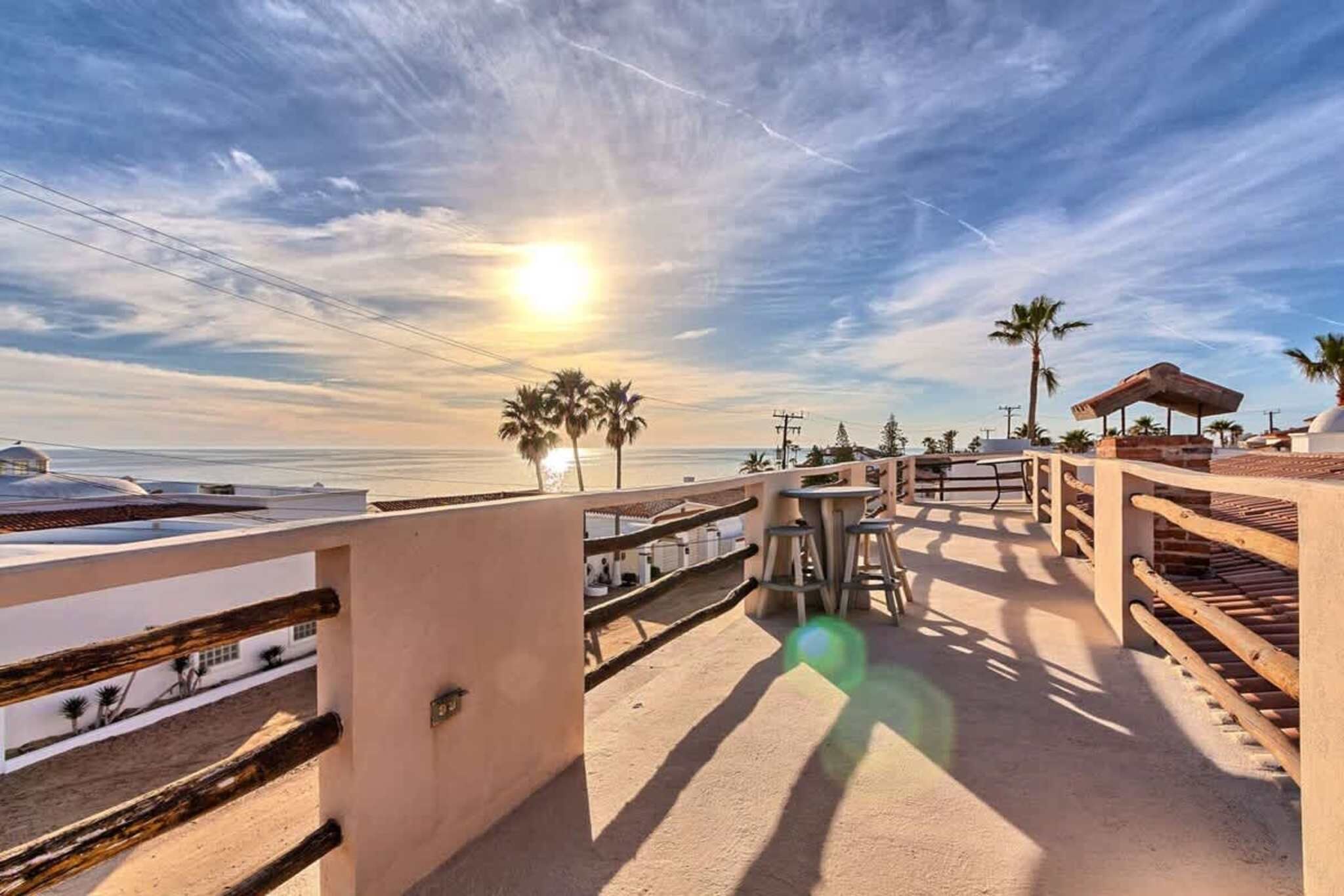 A beachside terrace with a view of the ocean, palm trees, and a wooden fence.