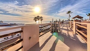 Une terrasse au bord de la plage, offrant une vue sur l’océan, les palmiers et une clôture en bois.