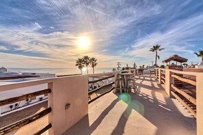 Eine Terrasse am Strand mit Blick auf das Meer, Palmen und einen Holzzaun.