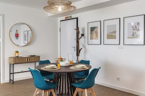 Een eethoek met een ronde tafel, teal stoelen en een houten console met een schaal en fruit.