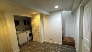 Une buanderie équipée d’un lave-linge et d’un sèche-linge, une porte donnant sur une autre pièce et un escalier en bois.