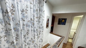 Un escalier avec des marches en bois et une rampe, menant à un palier avec un mur blanc et un tableau.