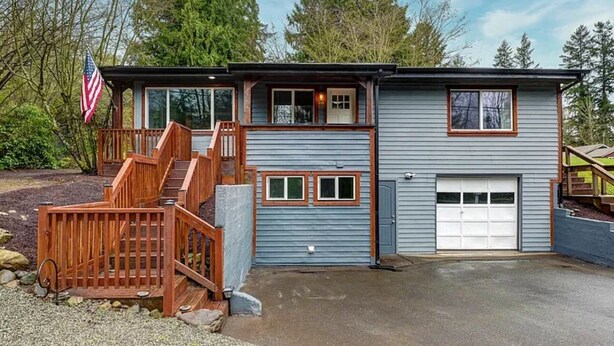 Une maison à deux étages avec un garage, une terrasse en bois et un drapeau américain.