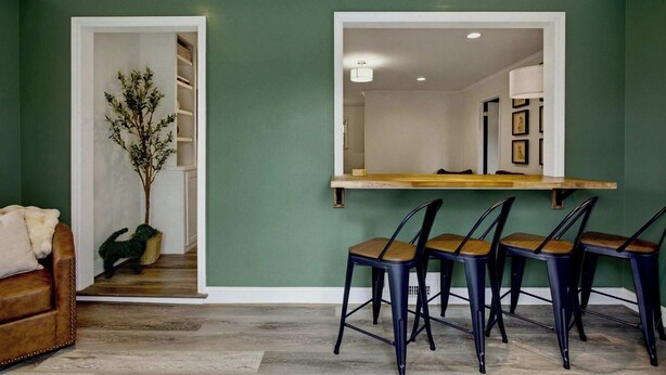 Un comedor con una mesa de madera y cuatro sillas, una planta en maceta y vista a una cocina.