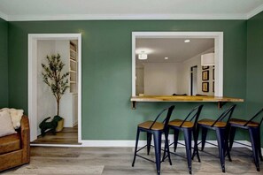Un coin repas avec une table en bois et quatre chaises, une plante en pot, et une vue sur la cuisine.