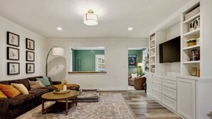 Una sala de estar con un sofá, una mesa de centro y un televisor sobre un mueble blanco.