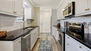 Una cocina con armarios blancos, encimera negra, electrodomésticos de acero inoxidable y alfombra estampada.