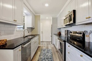 A kitchen with white cabinets, a black countertop, stainless steel appliances, and a patterned rug. - Dog’s Perfect Vacation｜54 Acres｜18 min Spring Hill (Columbia)