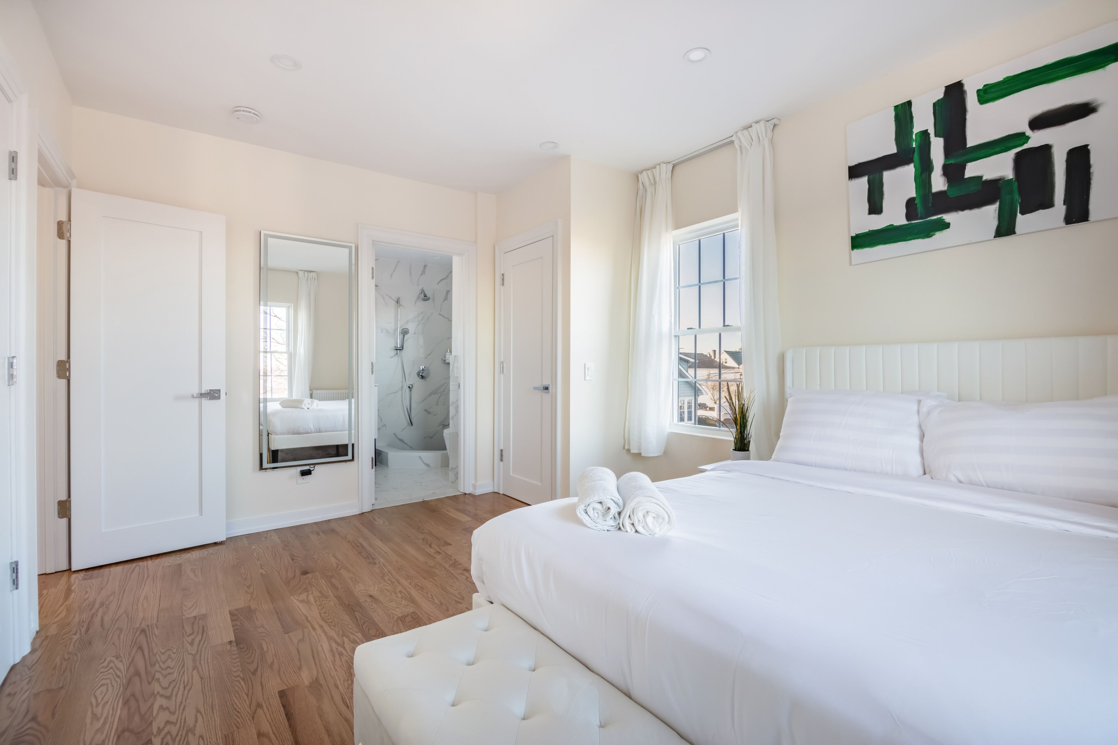Ein Schlafzimmer mit einem großen Bett, einem begehbaren Kleiderschrank, einem Badezimmer mit Dusche und einem Fenster mit Vorhängen.