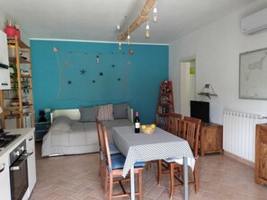 A cozy room with a dining table, chairs, a sofa, a bookshelf, and a kitchen area. - Lacona House (Lacona)
