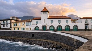 Un bâtiment situé sur la côte, doté d’une façade blanche, de portes vertes et d’un toit recouvert de tuiles rouges.