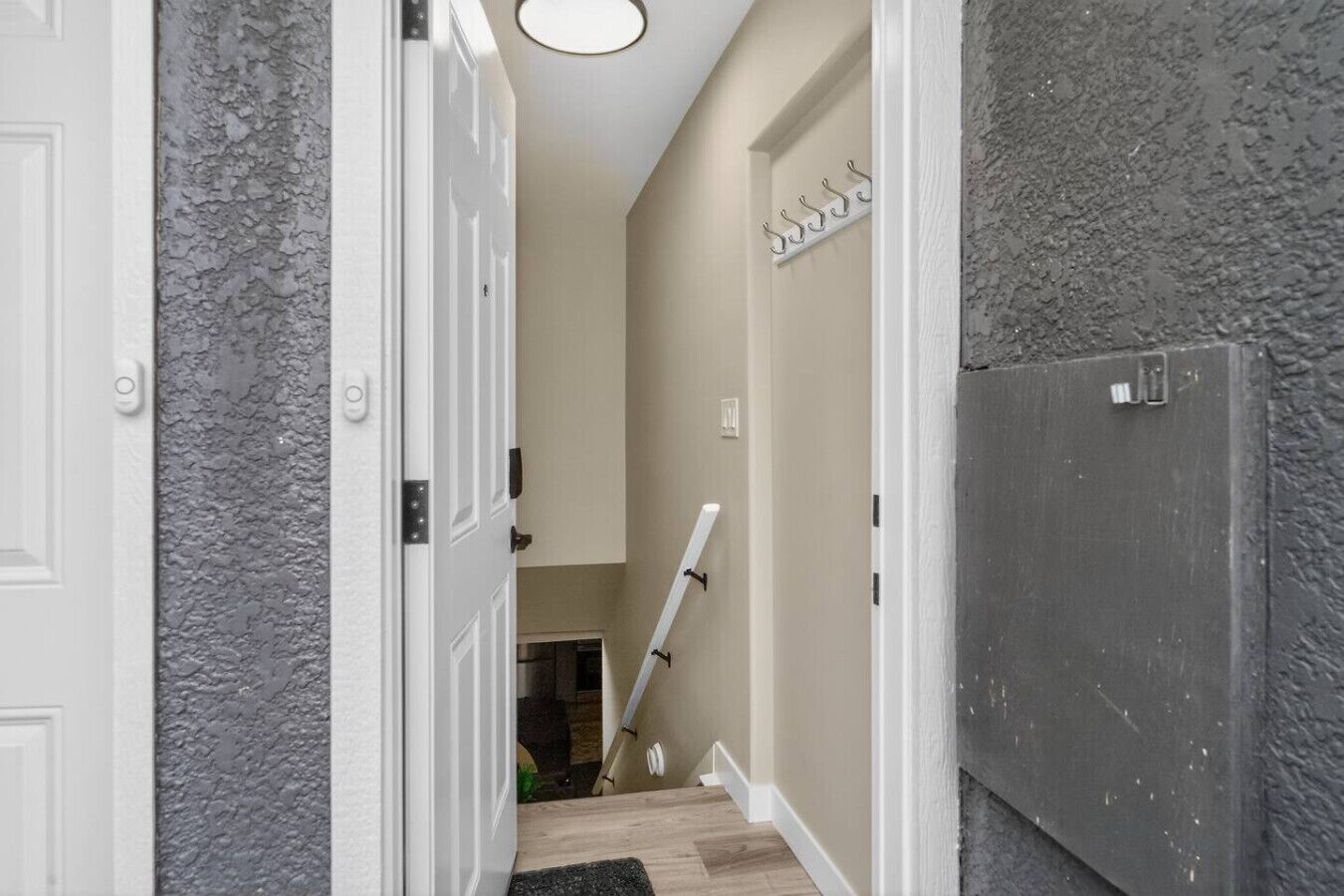 A narrow hallway with a white door, a gray textured wall, a white door frame, and a white door with a number plate.