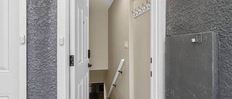 A narrow hallway with a white door, a gray textured wall, a white door frame, and a white door with a number plate.
