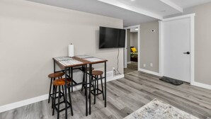Una sala de estar moderna con comedor, un televisor de pantalla plana en la pared y una puerta que da a otra habitación.