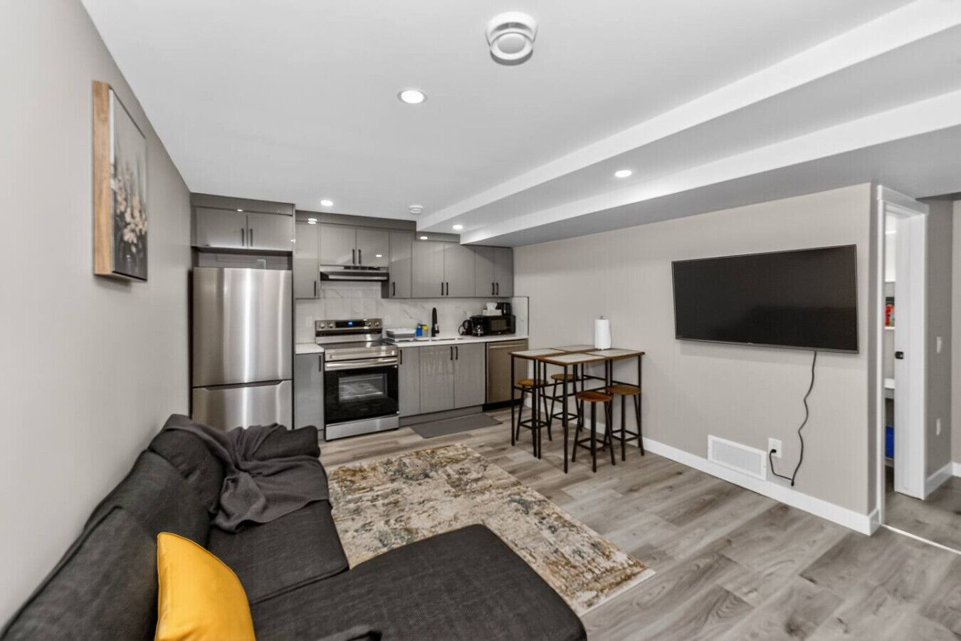 Eine moderne Wohnung mit Küchenzeile, Essbereich, Flachbildfernseher und einem grauen Sofa.