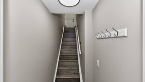 Una escalera estrecha con acabado de madera, un aplique en la pared y un perchero con ganchos.