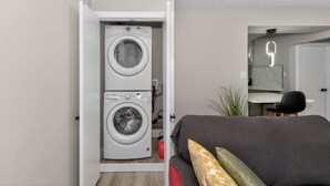 Una habitación pequeña con lavadora, cama, escritorio y espejo.