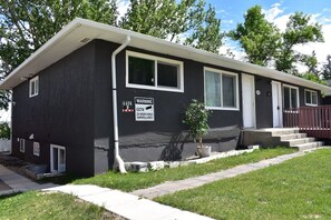 A single-story house with a dark exterior, a small front porch, and a warning sign for CCTV surveillance.