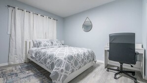 Un dormitorio con una cama, un escritorio, una silla, un espejo y una cortina.