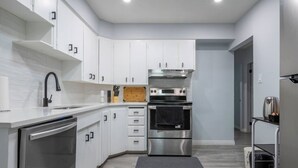 Una cocina moderna con armarios blancos, electrodomésticos de acero inoxidable y una tabla de cortar de madera.