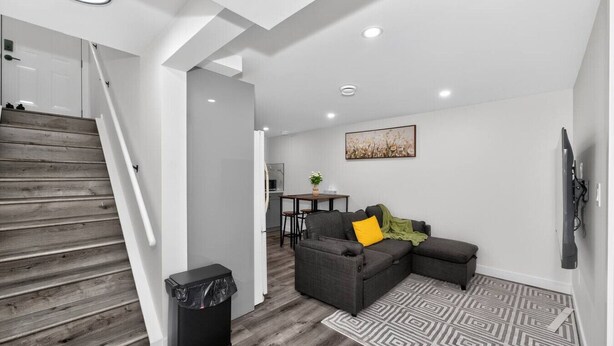 A modern living area with a staircase, grey sofa, and a TV. - Modern 2BR Basement Suite Near Downtown & Airport, SAIT, UofC | Ideal for Business Travel & Stampede Stays (Calgary)
