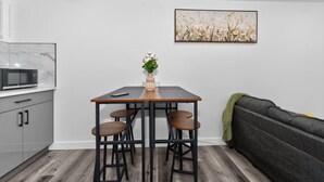 A compact kitchen with a microwave, a dining table with stools, and a sofa. - Modern 2BR Basement Suite Near Downtown & Airport, SAIT, UofC | Ideal for Business Travel & Stampede Stays (Calgary)