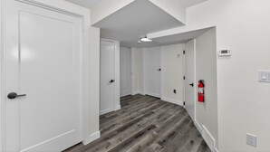 A hallway with white doors, a wooden floor, and a fire extinguisher on the wall. - Modern 2BR Basement Suite Near Downtown & Airport, SAIT, UofC | Ideal for Business Travel & Stampede Stays (Calgary)