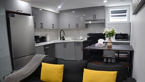 A modern kitchen with grey cabinets, a black stove, and a dining area with a table and chairs. - Modern 2BR Basement Suite Near Downtown & Airport, SAIT, UofC | Ideal for Business Travel & Stampede Stays (Calgary)