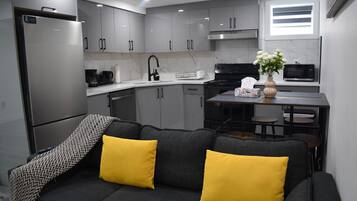 Een moderne keuken met grijze kastjes, een zwarte kookplaat en een eethoek met een tafel en stoelen.