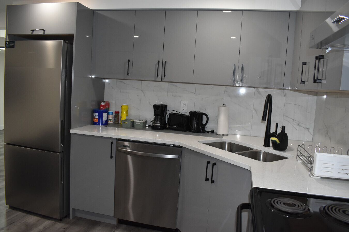 Een moderne keuken met roestvrijstalen apparatuur, grijze kastjes en een marmeren spatwand.