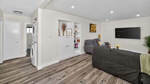Een moderne woonkamer met een grijze bank, een wit kastje en een flatscreen televisie aan de muur.