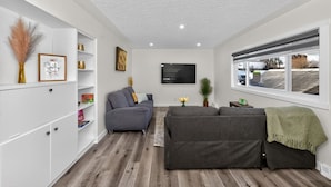 Een moderne woonkamer met een grijze bank, witte planken en een raam met uitzicht.