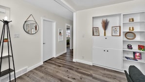 Een hal met een witte muur, een spiegel, een zwart vloerlamp en een wit wandrek met decoratieve objecten.