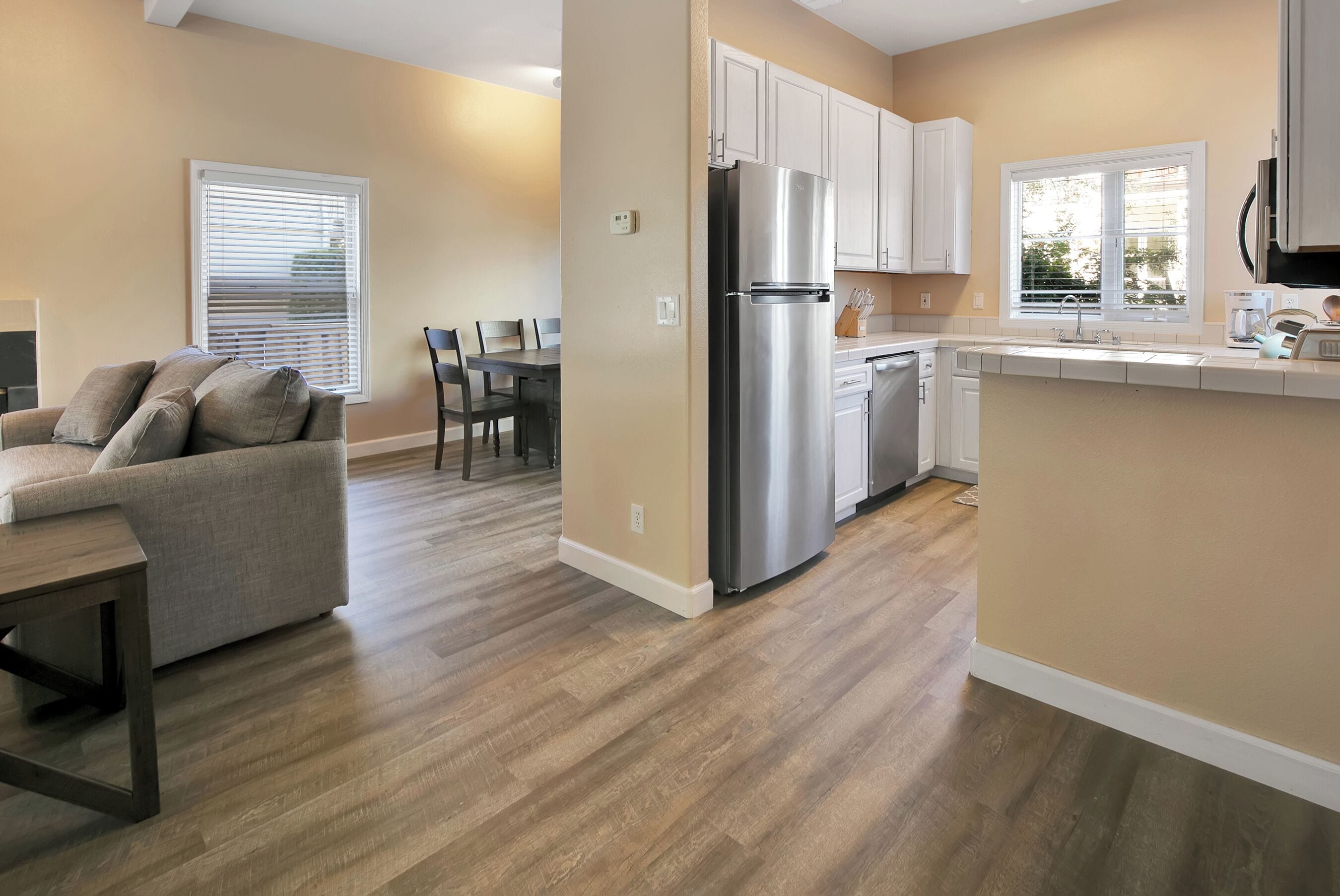 A modern kitchen with a stainless steel refrigerator, white cabinets, and a wooden floor.