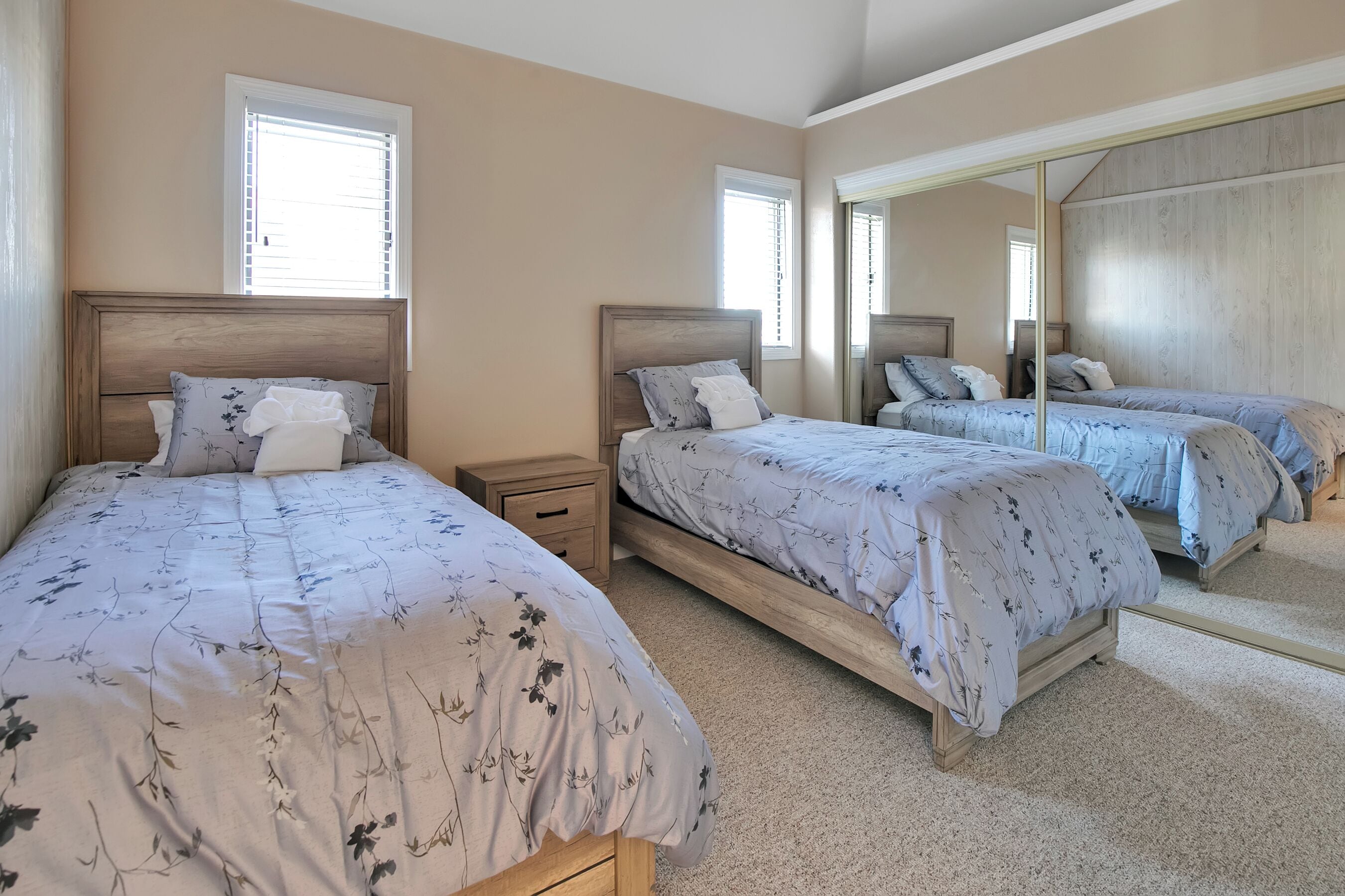 A bedroom with two beds, a nightstand, and a large mirror.