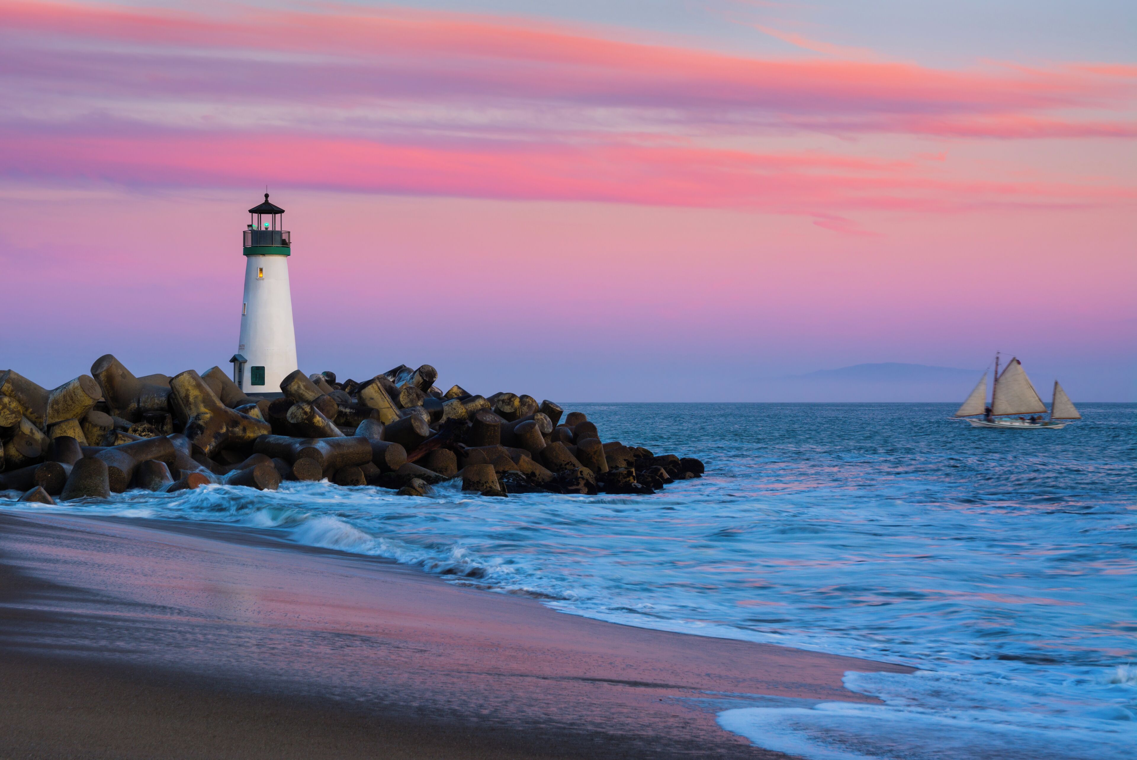 A lighthouse on a rocky outcrop by the sea with waves crashing against it.