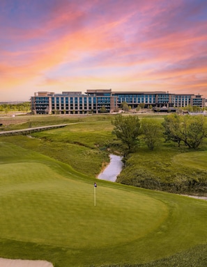 A golf course with a flagstick, a building with multiple floors, and a river running through the landscape. - THE ELITE ESCAPE Modern luxury with Cozy Comfort (Frisco)
