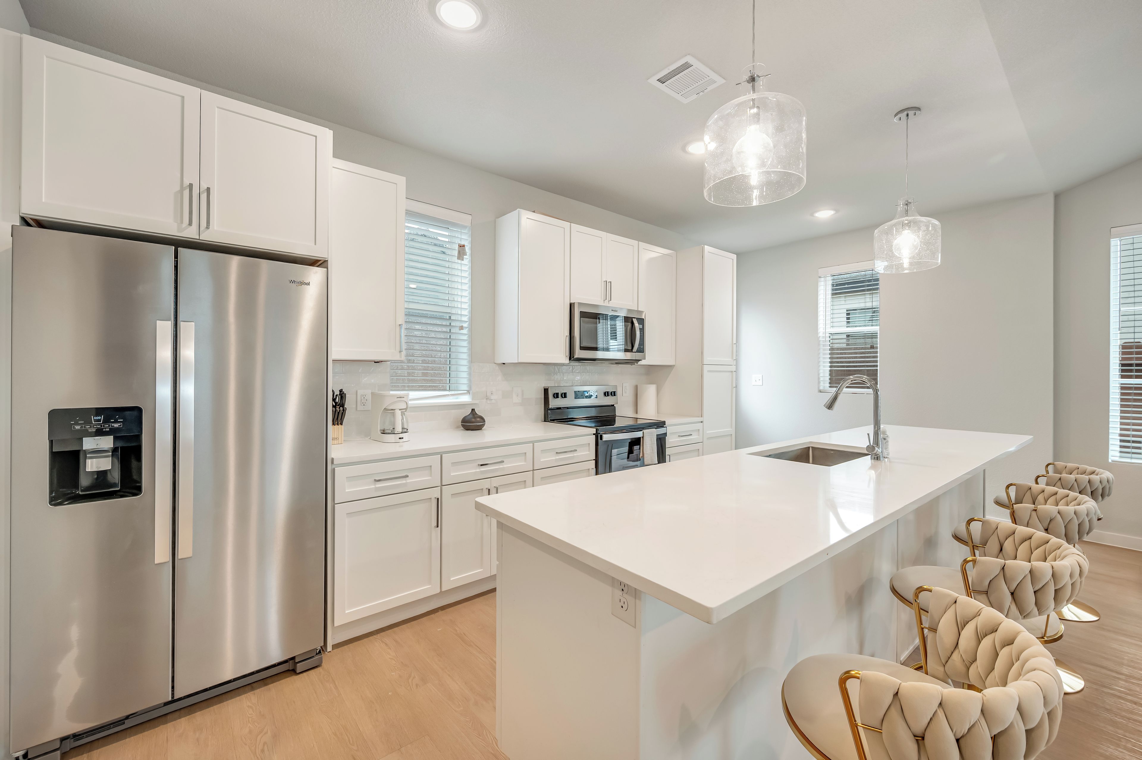 A modern kitchen with a stainless steel refrigerator, a built-in microwave, and a large island with bar stools.