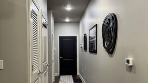 A hallway with a dark wood floor, white walls, a black door at the end, and a ceiling light.